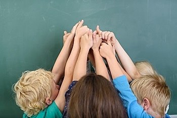Kids Raising their Arms at the Center together and Showing Thumbs Up Hand Signs Against Green Chalkboard.
