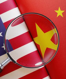 American and Chinese flag pair under a magnifier. Horizontal composition with copy space and selective focus.