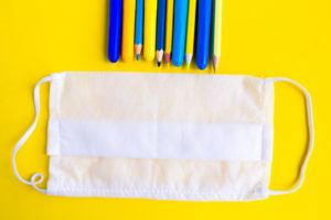 Color pencils and medical mask on bright yellow background. Back to school concept. School quarantine concept