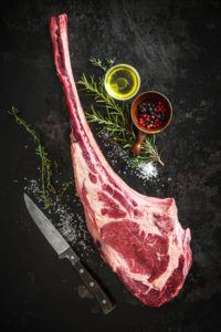 Dry aged raw tomahawk beef steak with ingredients for grilling:
