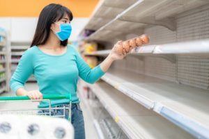 Asian woman pick up last egg pack at Supermarket empty shelves amid COVID 19 coronavirus fears, shoppers panic buying and stockpiling toilet paper preparing for a pandemic.