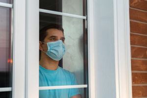Young man in medical mask is looking out window. Coronavirus pandemic. Home quarantine, self isolation because of the Coronavirus disease, COVID 19. Man in medical mask stay at home. Self isolation.