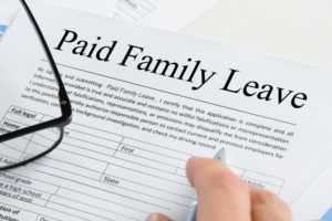 Close up Of A Person's Hand Holding Pen Over Paid Family Leave Form With Spectacles