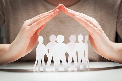 Paper people under hands in gesture of protection. Concept of insurance, social protection and support.