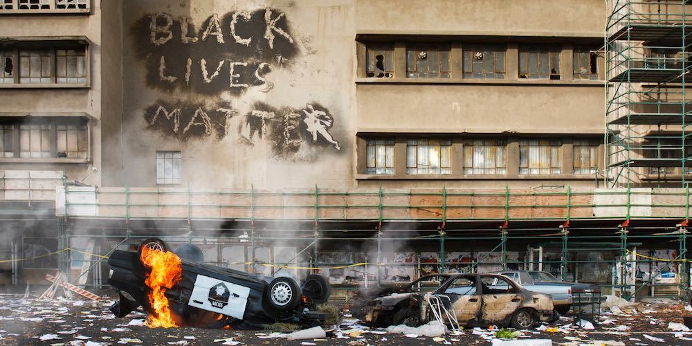 Black Lives Matter protest riot vandalism, looting aftermath concept, flaming police car smashed, overturned with black lives matter text slogan message on building. Excessive force, police brutality