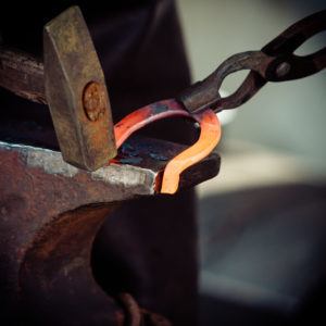 Making decorative element in the smithy on the anvil. Hammering glowing steel. Blacksmith forges a hot horseshoe.