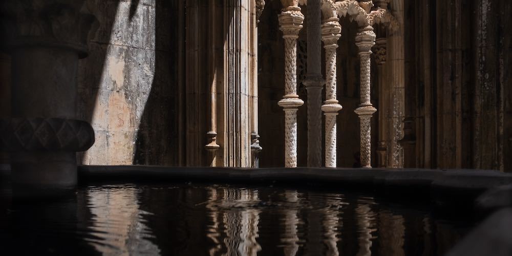 Batalha, Portugal 07 08 2020: Architectural details inside the Monastery of Batalha reflect in the water basin of the fountain. Late Gothic architecture in Portugal.