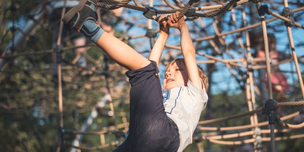 A 5 year old boy climbs on the ropes at the playground