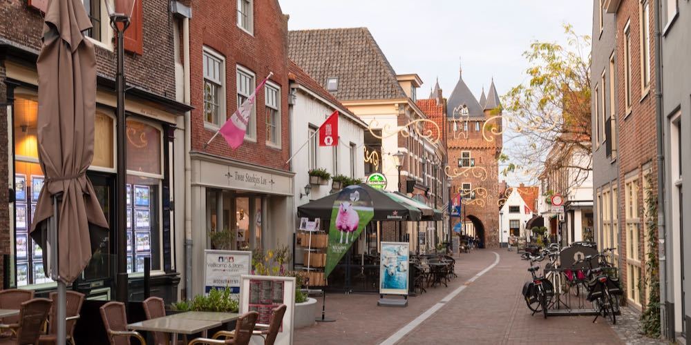 Hattem, Netherlands, November 8, 2022; Cozy street with shops and small eateries with the 14th century city gate in the background in the picturesque medieval Dutch fortified town of Hattem.