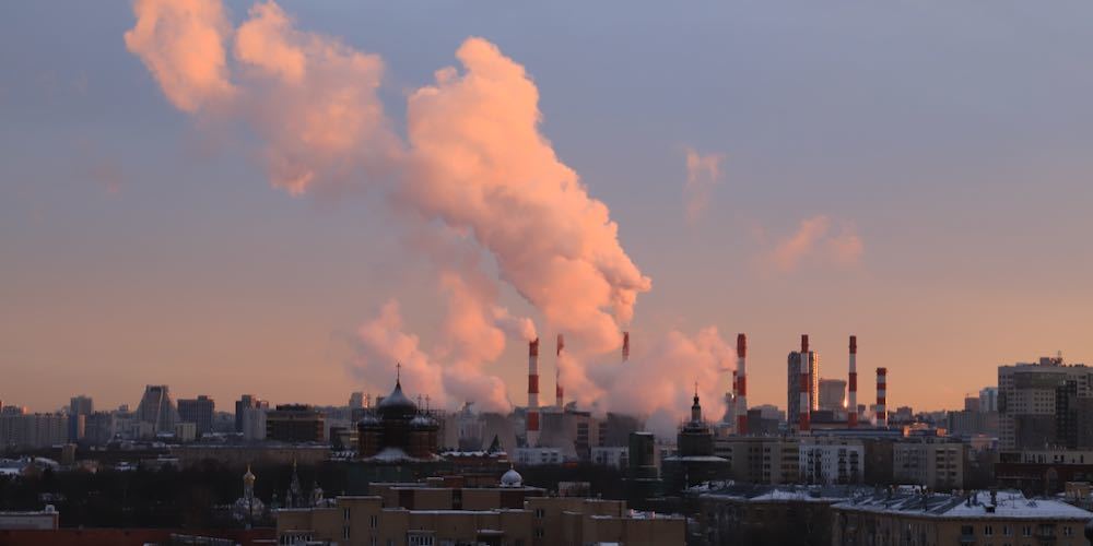 Evening panorama of one of the residential areas of Moscow and the chimneys of a thermal power plant with pink smoke rising high into the sky and illuminated by the setting sun.