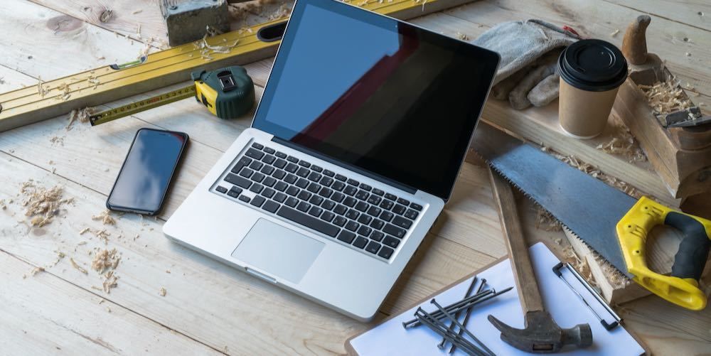 Close up laptop on wooden planks, smartphone, clipboard, pen, nails, hammer, plane, saw, tape measure, level, gloves, glasses, cup of coffee, sawdust. Carpentry. Mock up. Construction business.