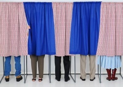 A row of five voting booths with men and women casting their ballots at a polling place. Horizontal format, only showing the legs of the voters, people are unrecognizable..