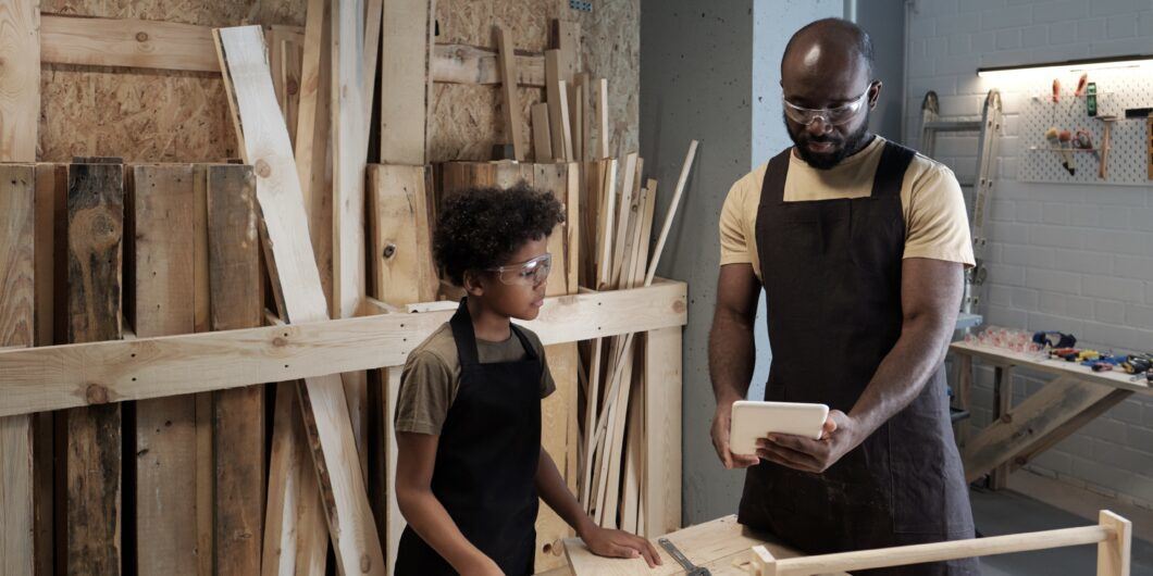 Portrait of African American father teaching son carpentry while working together in woodworking shop
