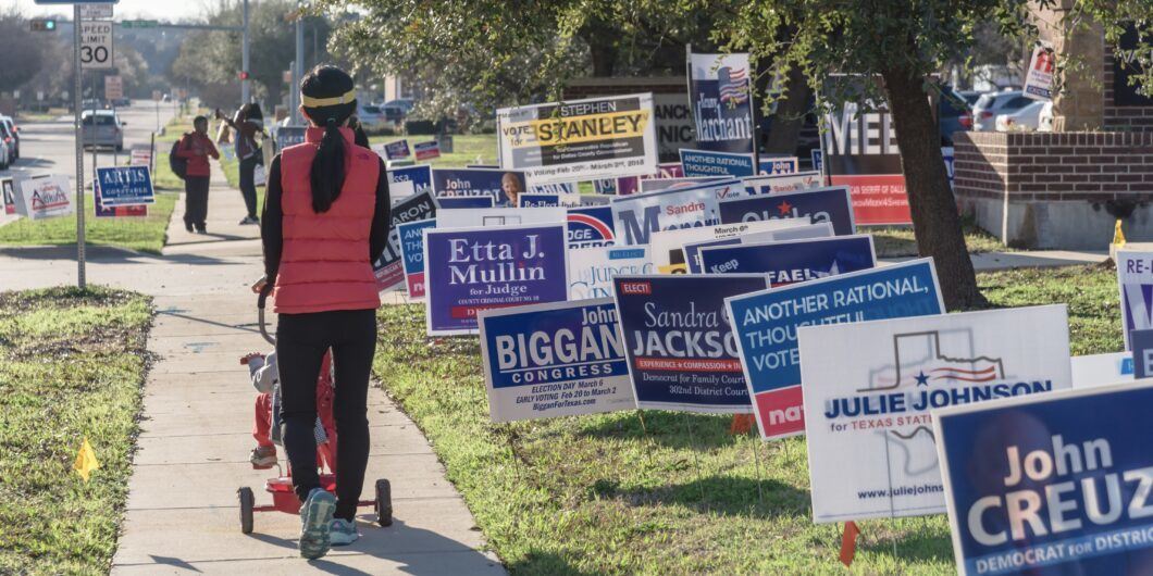 IRVING, TEXAS, USA MAR 2, 2018: Yard sign at residential street near library for primary election day in Dallas county. Rear view of young Asian lady with stroller on concrete pathway