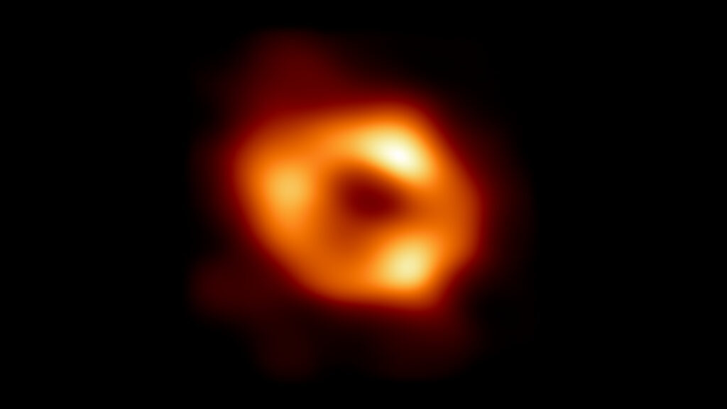 This is the first image of Sgr A*, the supermassive black hole at the centre of our galaxy, with an added black background to fit wider screens. It’s the first direct visual evidence of the presence of this black hole. It was captured by the Event Horizon Telescope (EHT), an array which linked together eight existing radio observatories across the planet to form a single “Earth sized” virtual telescope. The telescope is named after the event horizon, the boundary of the black hole beyond which no light can escape.   Although we cannot see the event horizon itself, because it cannot emit light, glowing gas orbiting around the black hole reveals a telltale signature: a dark central region (called a shadow) surrounded by a bright ring like structure. The new view captures light bent by the powerful gravity of the black hole, which is four million times more massive than our Sun. The image of the Sgr A* black hole is an average of the different images the EHT Collaboration has extracted from its 2017 observations.  In addition to other facilities, the EHT network of radio observatories that made this image possible includes the Atacama Large Millimeter/submillimeter Array (ALMA) and the Atacama Pathfinder EXperiment (APEX) in the Atacama Desert in Chile, co owned and co operated by ESO is a partner on behalf of its member states in Europe.