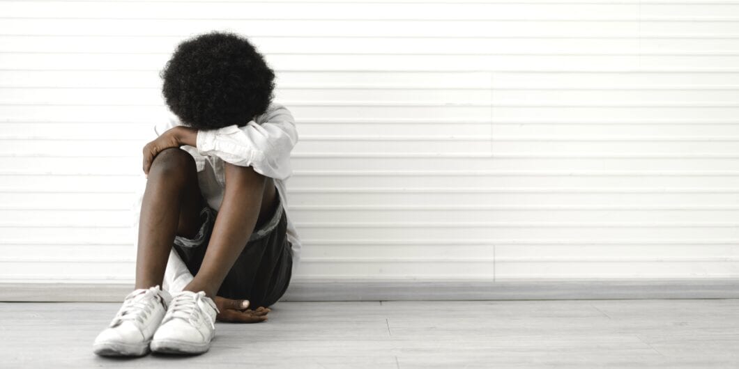 Portrait of sad depressed black african american cute little boy child alone sitting on floor at home