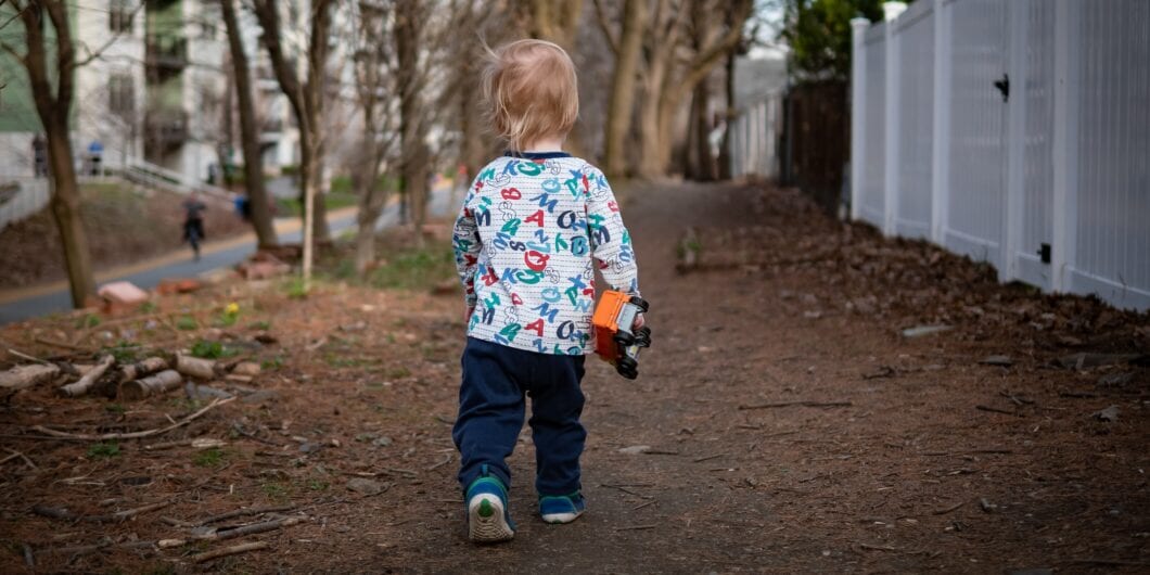 Toddler with a toy truck in his hand walking along a public community path in Somerville, MA, USA.