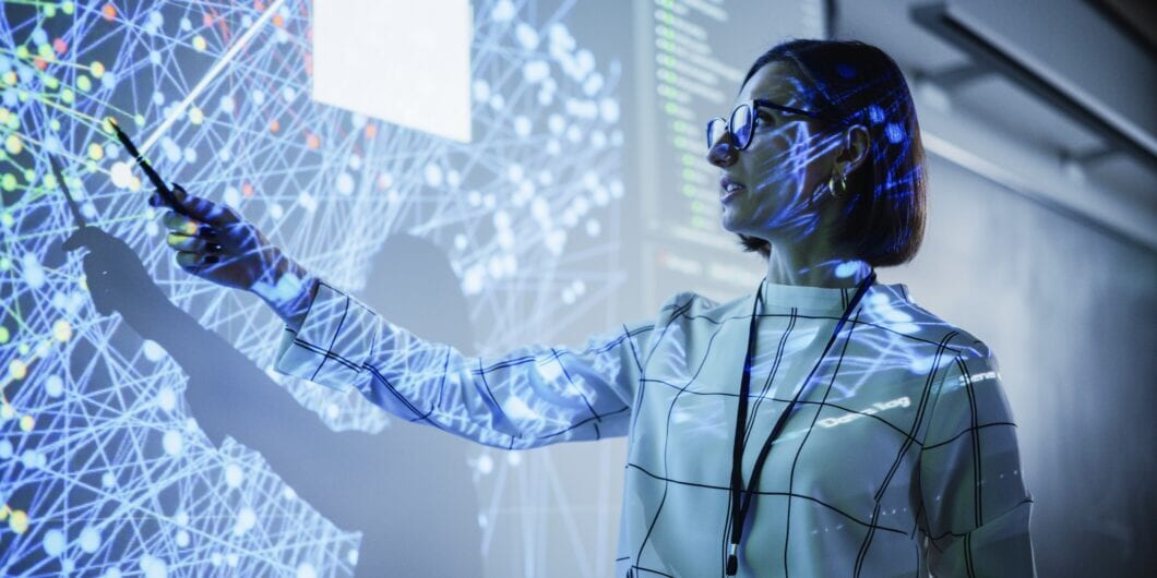 Young Female Teacher Giving a Data Science Presentation in a Dark Auditorium with Projecting Slideshow with Artificial Intelligence Neural Network Architecture. Business Startup and Education Concept