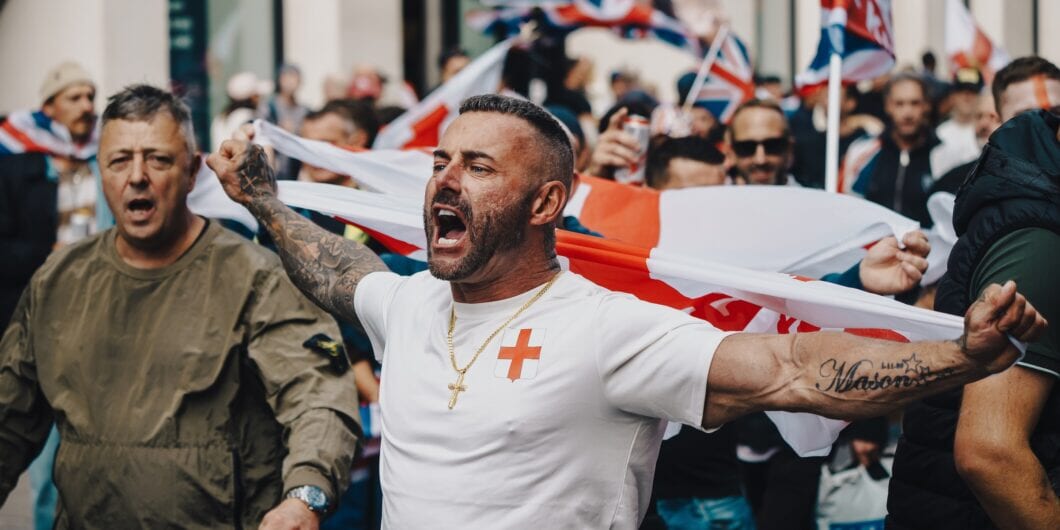 London, UK – 2025.09.13 – A demonstrator in a St. George’s Cross shirt passionately shouts while holding an English flag at a free speech protest, surrounded by a crowd of supporters.
